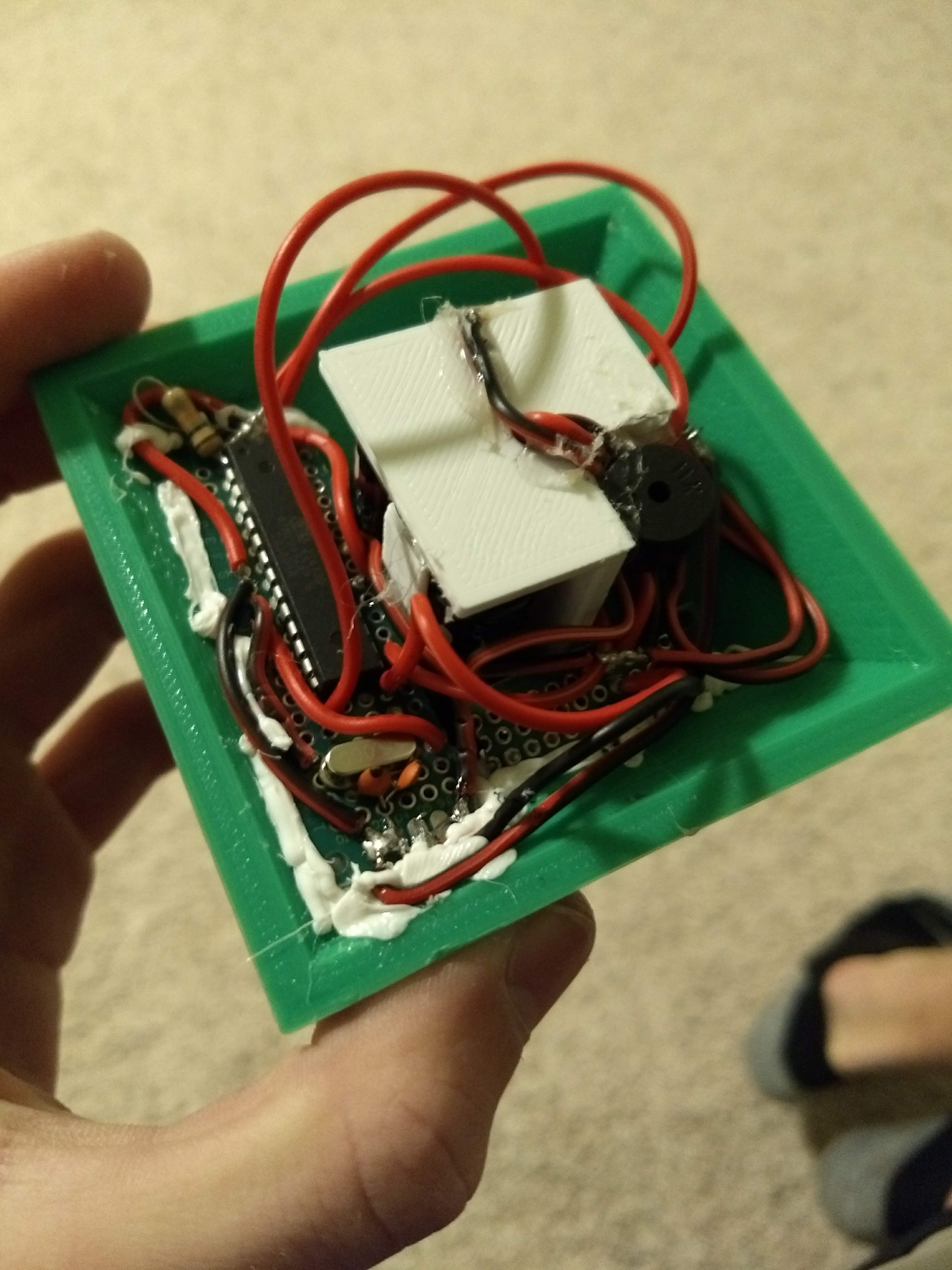 The underside of the tree ornament with the cover removed showing exposed wires, a microcontroller, and other components with 3D-printed and hot glue connections