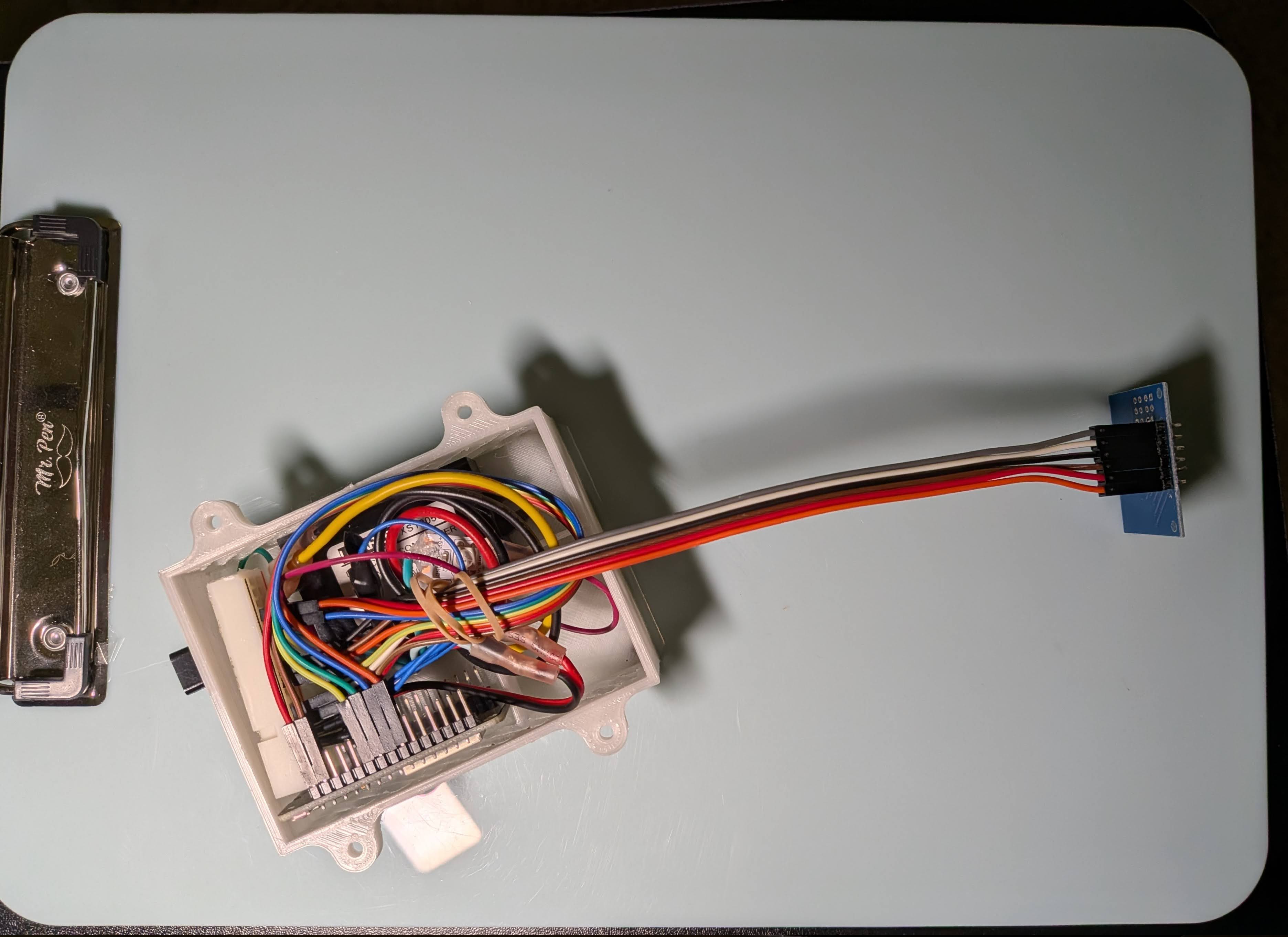 The electronic components and wires are stuffed close in a 3D printed plastic housing, with the capacitive touch sensor leading out of the housing